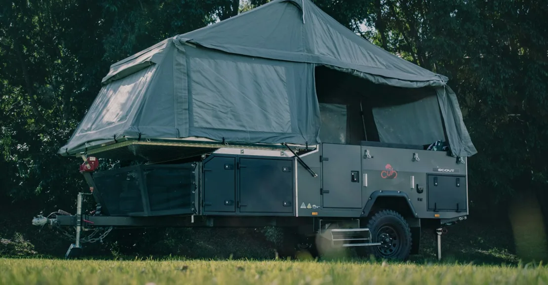 A dark green pop-up camper trailer with its canvas sides and roof fully extended.
