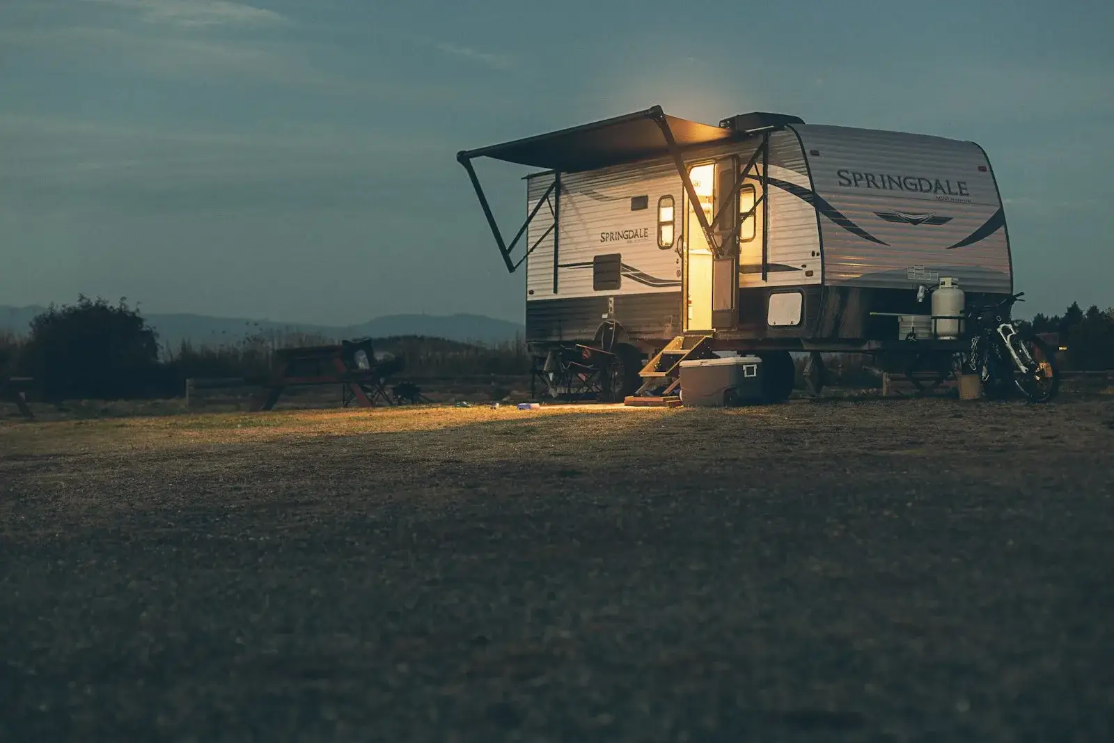 A travel trailer parked in a field at night with its interior lights on and awning extended.